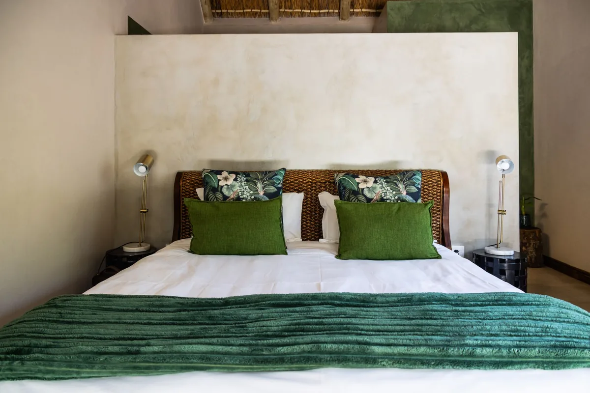 A neatly made double bed with green cushions and a green throw between two brass reading lamps
