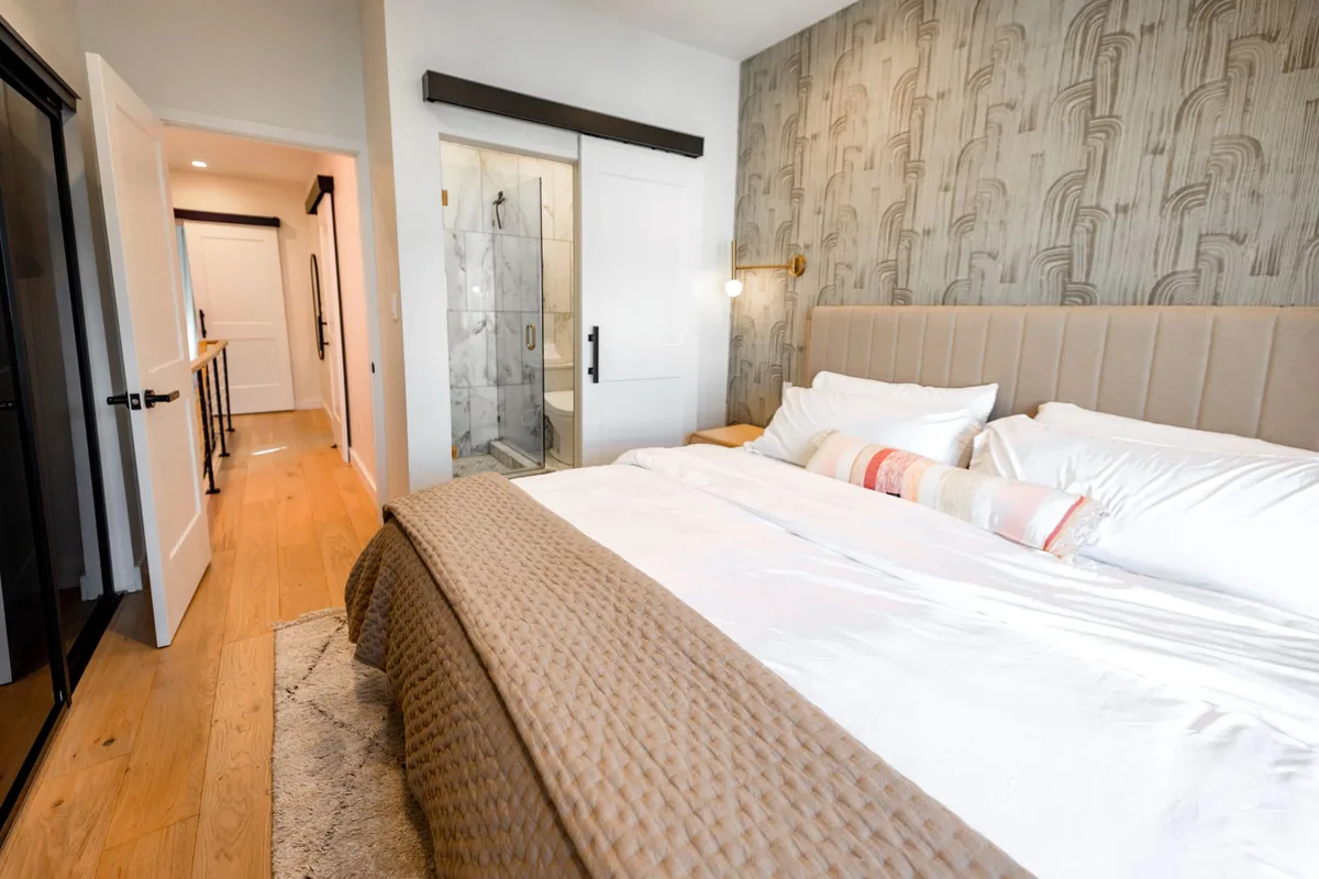 A wide made bed in a bedroom with an open door to a hallway and a sliding door to a bathroom