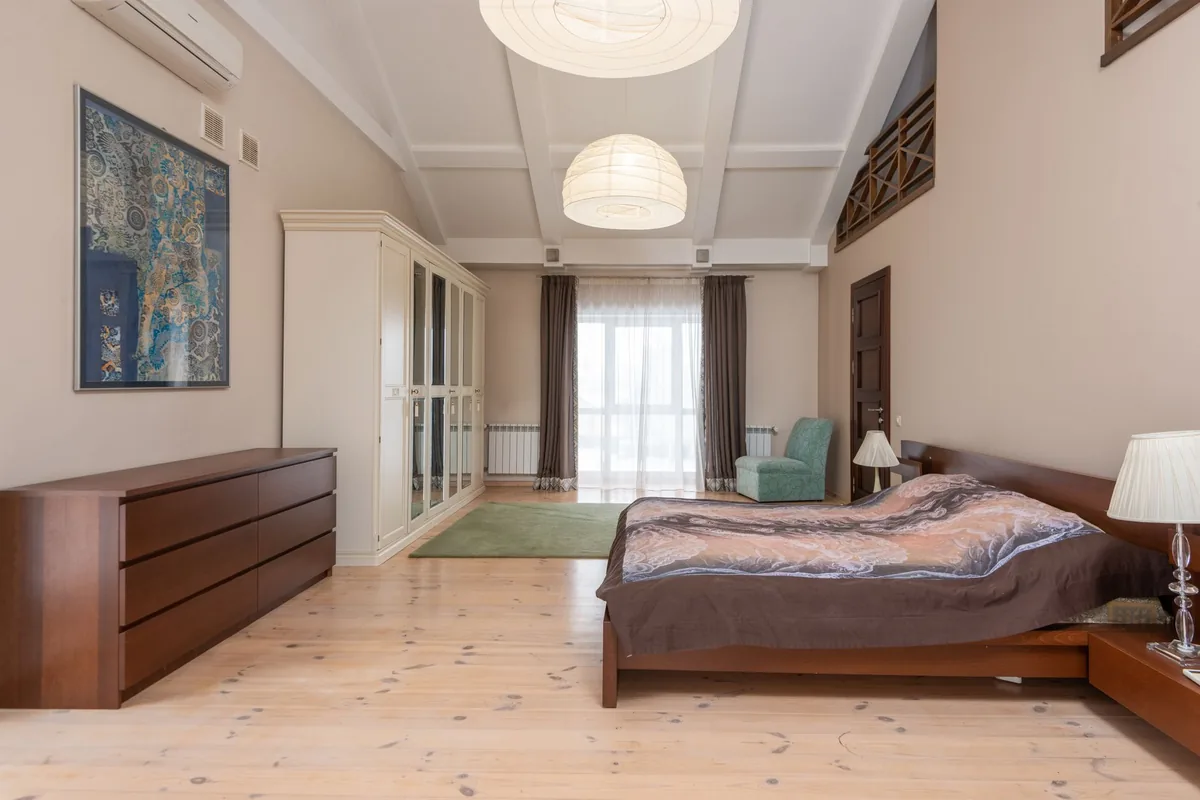A large bedroom with a low wooden bed, a long chest of drawers, a mirrored wardrobe and open floor beside the bed