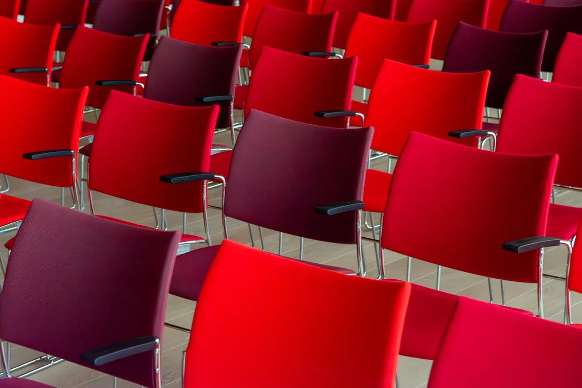 Rows of red and burgundy upholstered chairs with black armrests on a pale wood floor