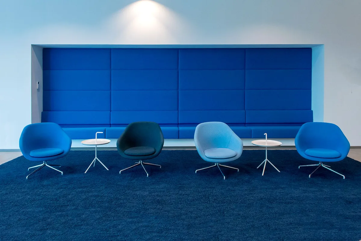 Four rounded lounge chairs in shades of blue with small white side tables on a navy carpet in a lobby