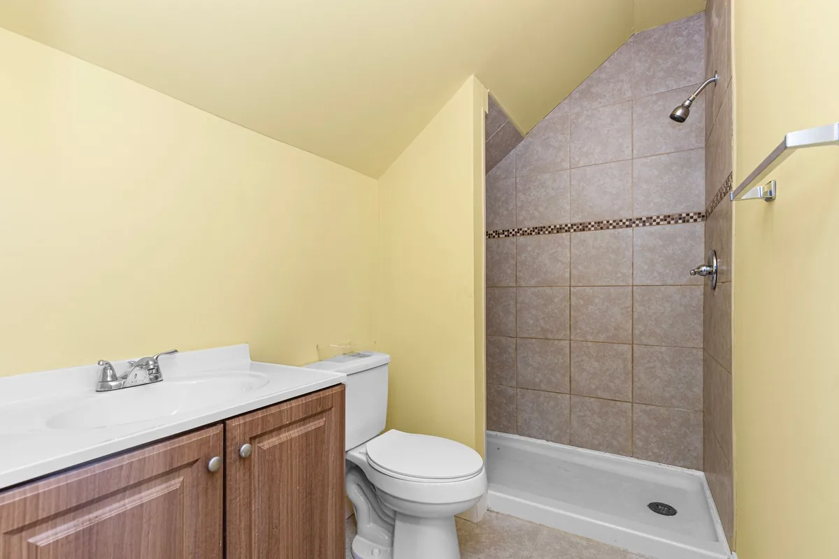 A compact bathroom with pale yellow walls, a vanity, a toilet and a tiled shower stall with a low white base
