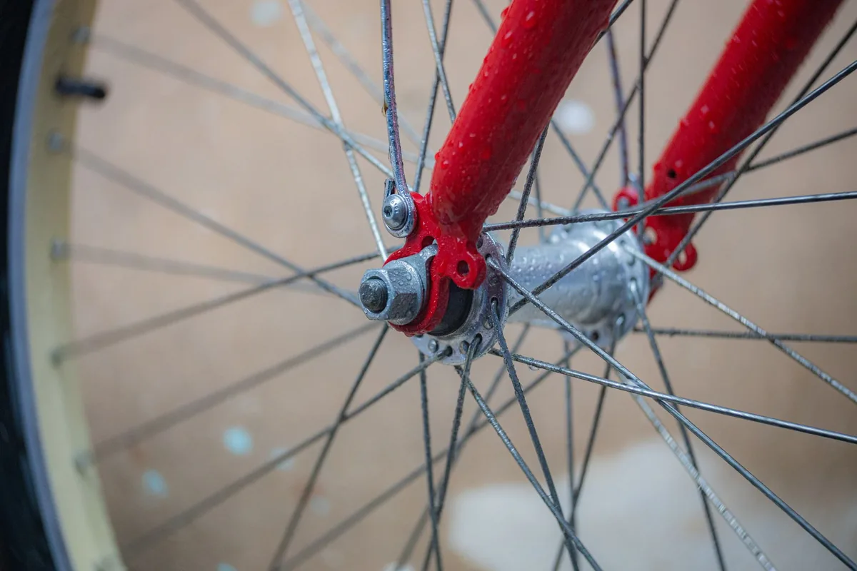 Close-up of a wet bicycle wheel with silver spokes beside a red front fork