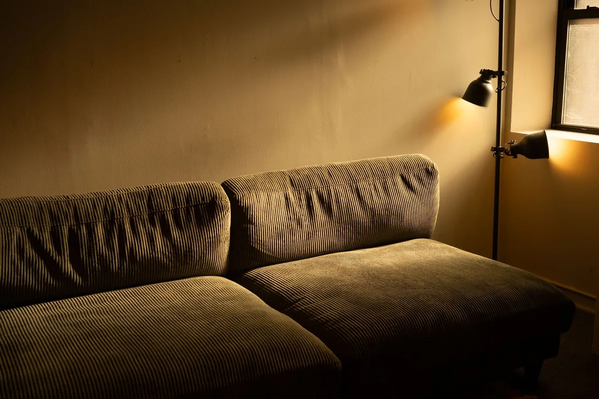 A deep corduroy sofa with two thick seat cushions under a floor lamp in a warmly lit room