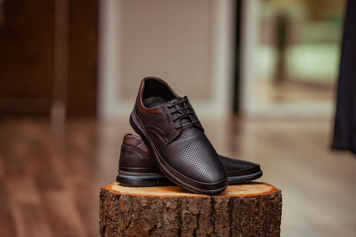 A pair of dark brown perforated leather lace-up shoes on a tree stump