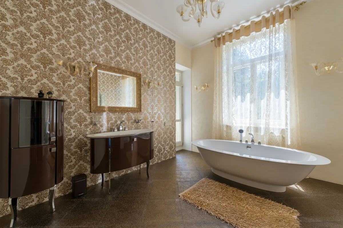 A long beige shag mat on a dark tiled floor beside a freestanding white bathtub under a tall curtained window