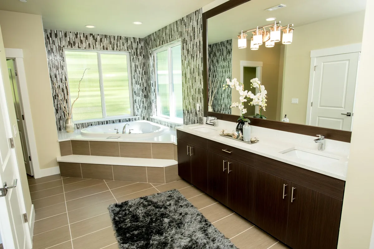 A dark grey shag rug on a beige tiled bathroom floor in front of a long double vanity and a corner tub