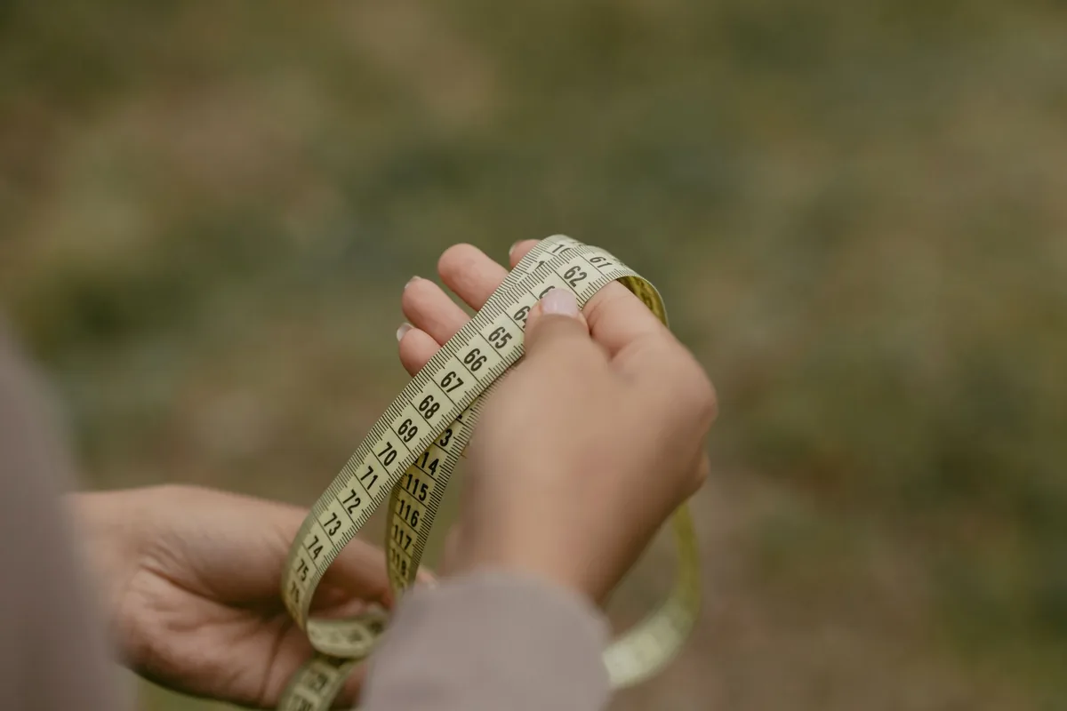Two hands holding a loop of soft measuring tape marked in centimetres