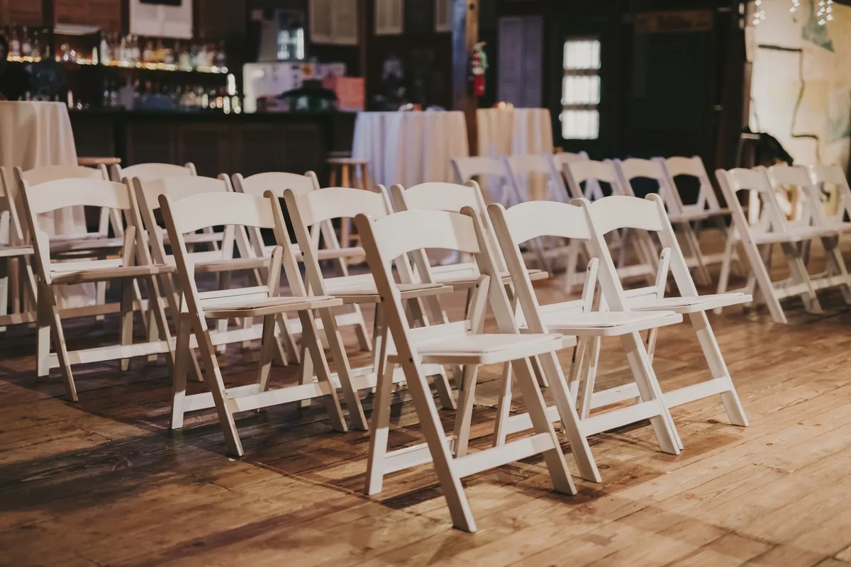 Rows of white folding chairs with padded seats set out on a wooden floor in an event room