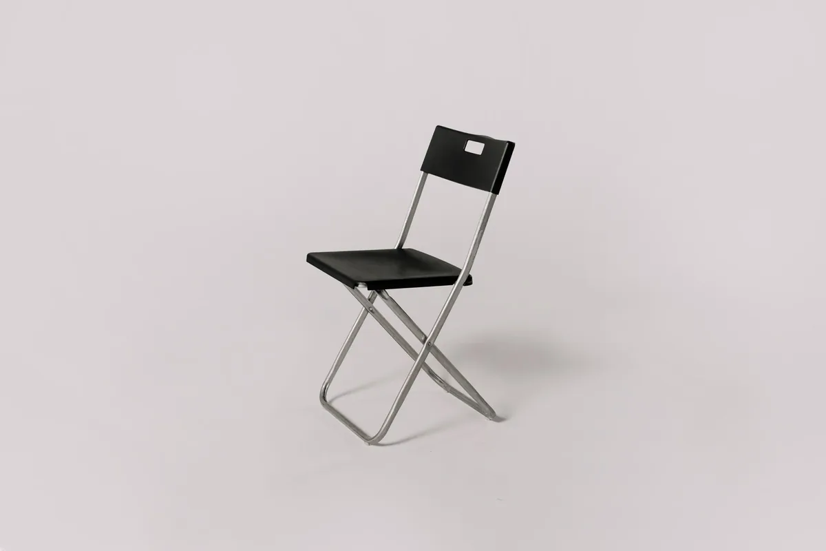 A single black folding chair with a steel frame standing against a plain gray background