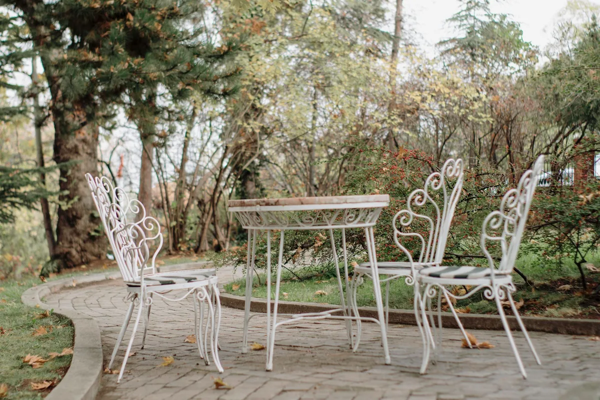 White metal garden chairs with striped seat cushions around a small round table on a brick patio