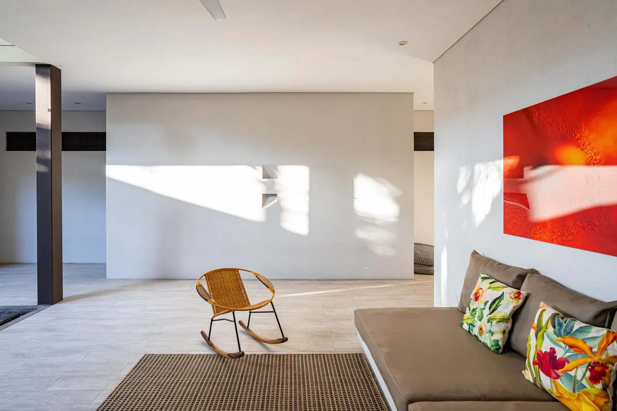 A woven rocking chair with curved wooden rockers on a pale tiled floor in a bright, sparsely furnished living room