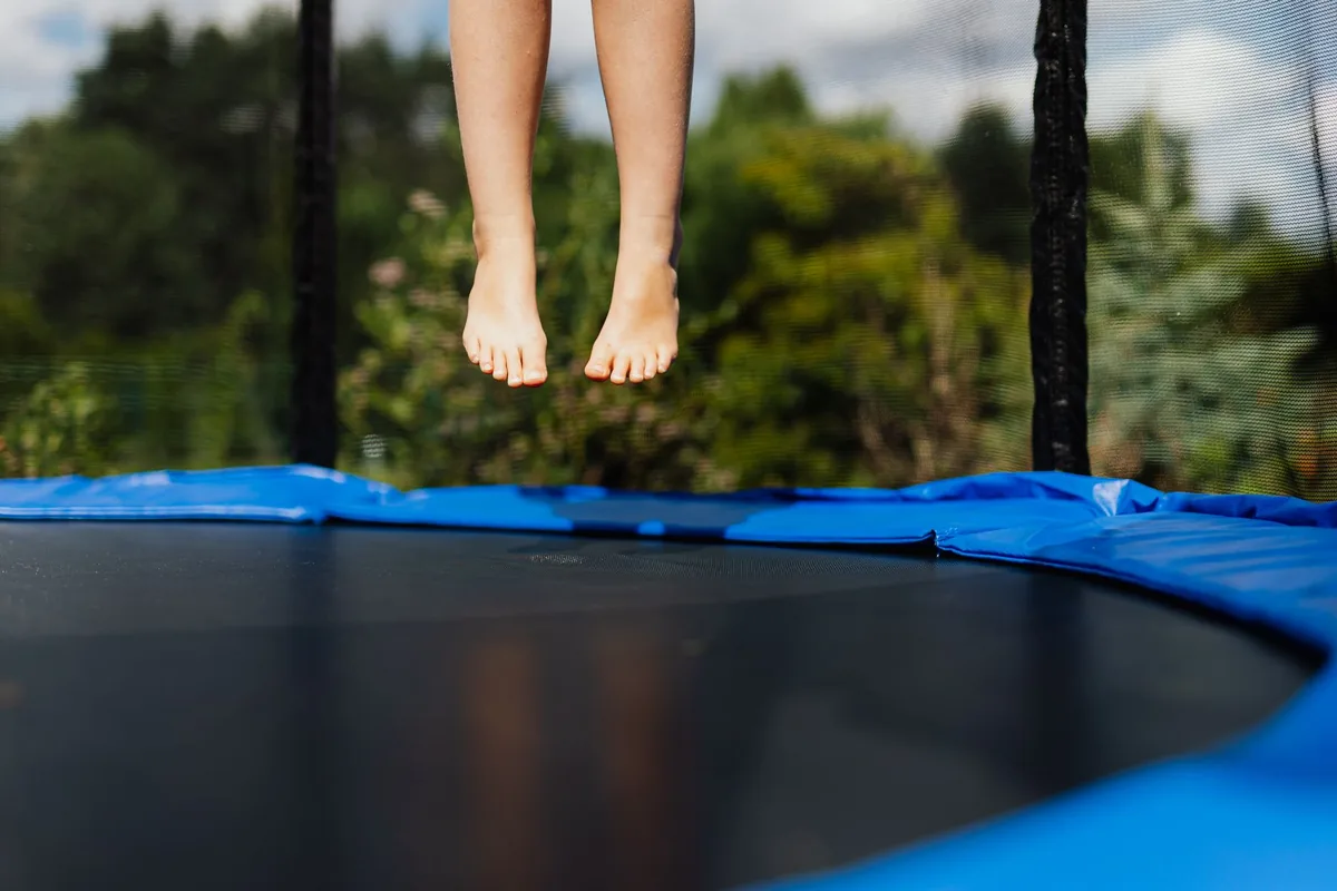 Bare feet in mid-air above a black trampoline mat with a blue edge pad and a safety net behind