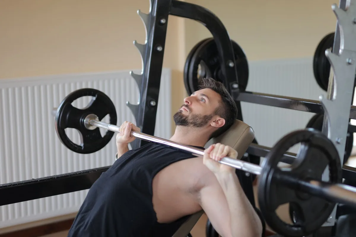 A man pressing a loaded barbell from an incline bench set inside a squat rack