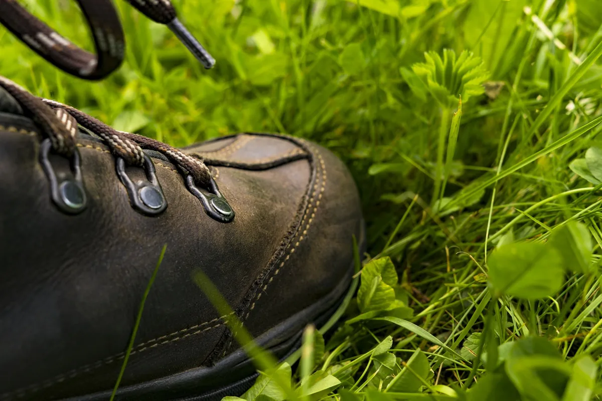 Close-up of the toe of a dark leather hiking boot with patterned laces standing in green grass