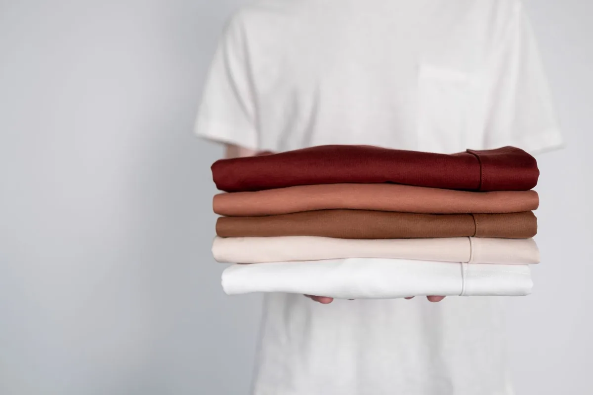Hands holding a stack of folded tops in red, brown and white