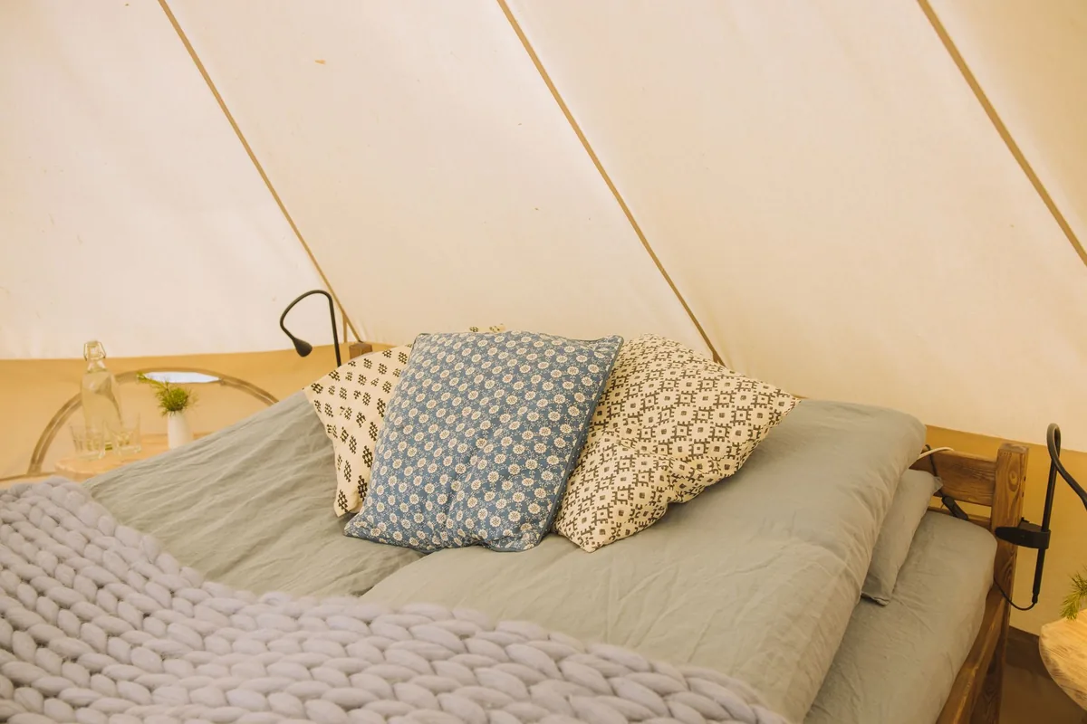 A chunky knit blanket over the foot of a bed with patterned pillows, inside a canvas tent