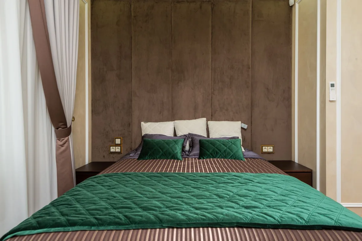 A bedroom with a green quilted bedspread and a padded headboard