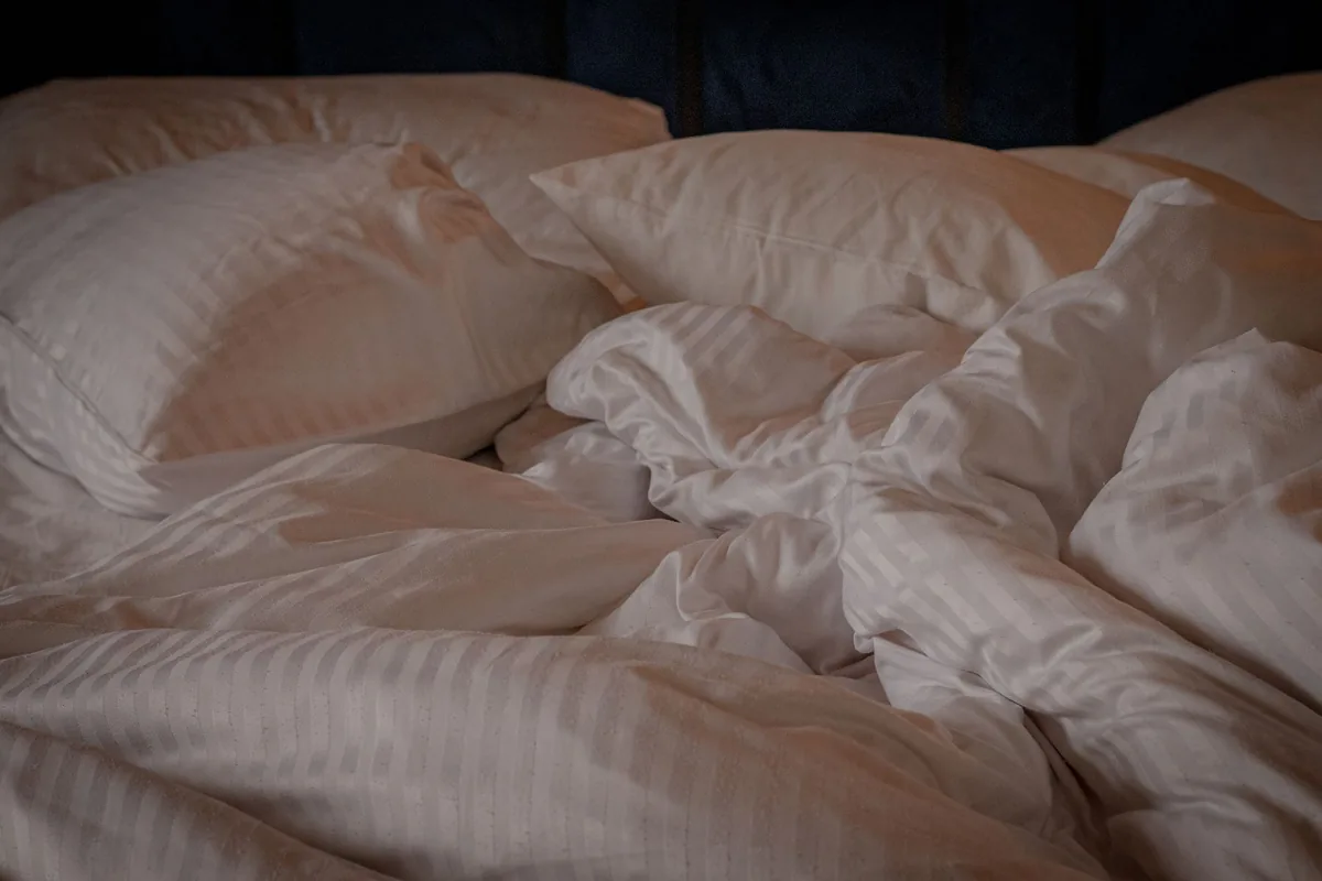 A rumpled white duvet and pillows on an unmade bed