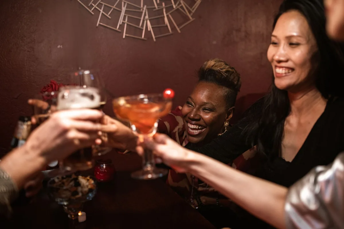 Friends raising cocktail glasses across a table in a dim bar