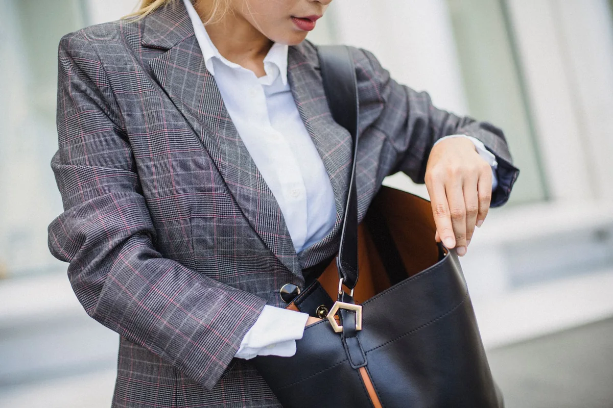 A woman in a grey plaid blazer and white shirt reaching into a black shoulder bag
