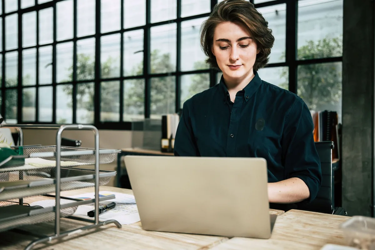 A woman in a dark button-up shirt working on a laptop in an office