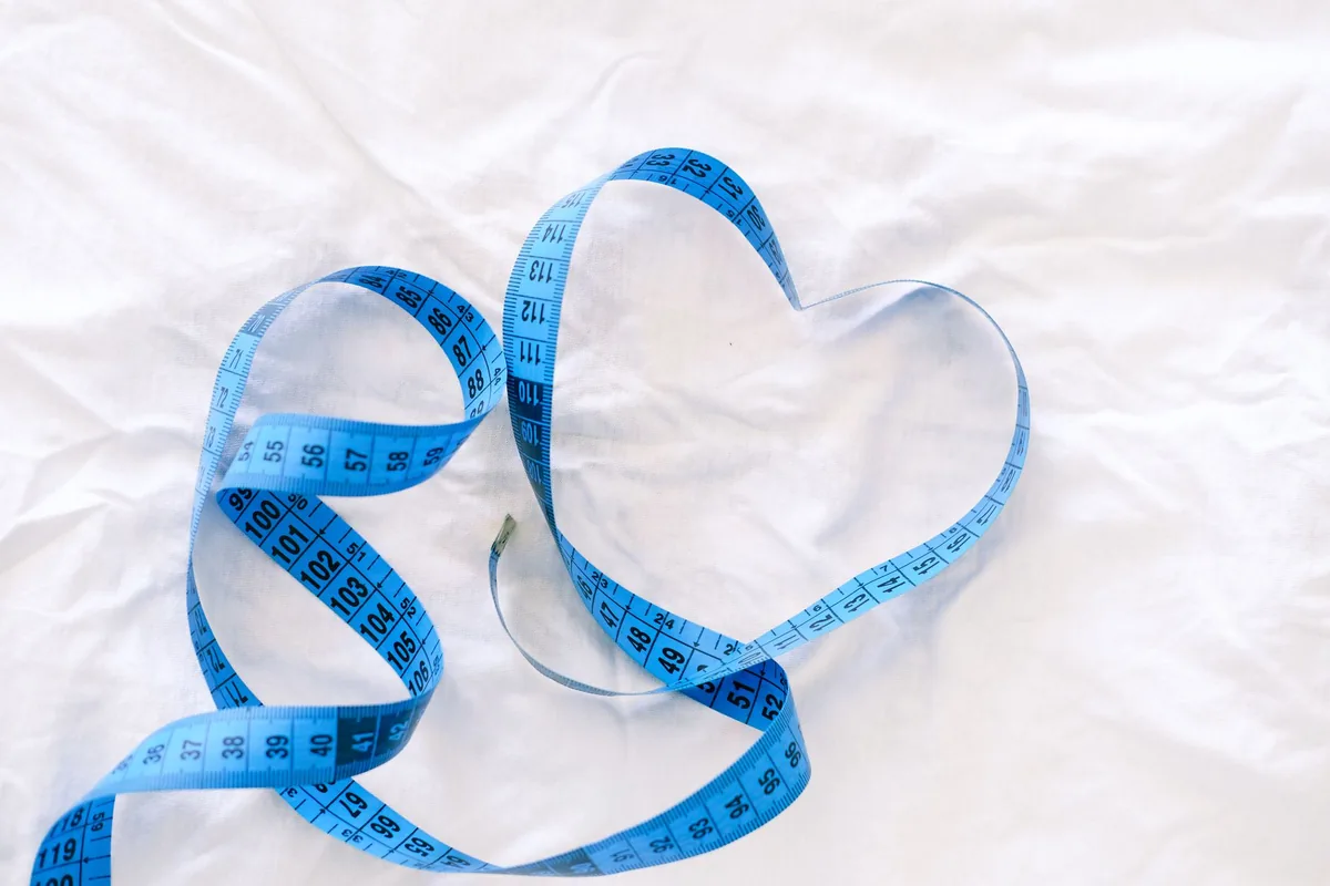 A blue measuring tape curled into a heart shape on white fabric