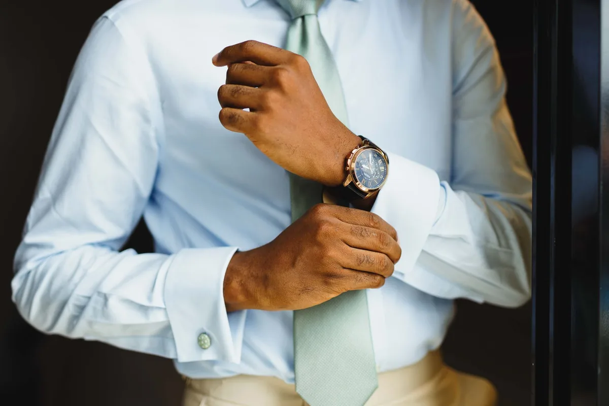 A man in a pale blue dress shirt fastening his cuff