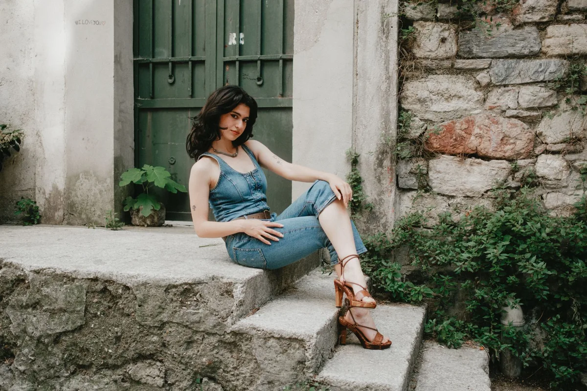 A woman in denim sitting on stone steps beside a green door
