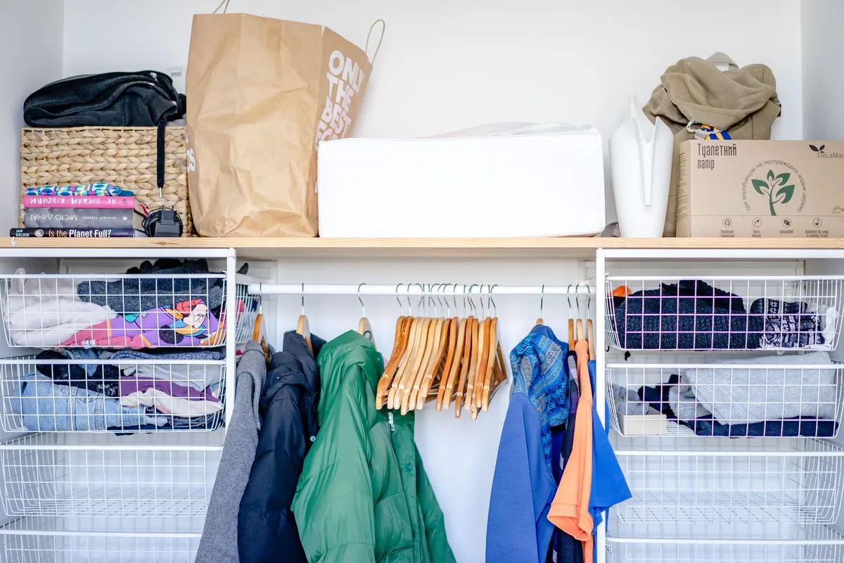 An open wardrobe with folded clothes, hanging jackets and storage baskets