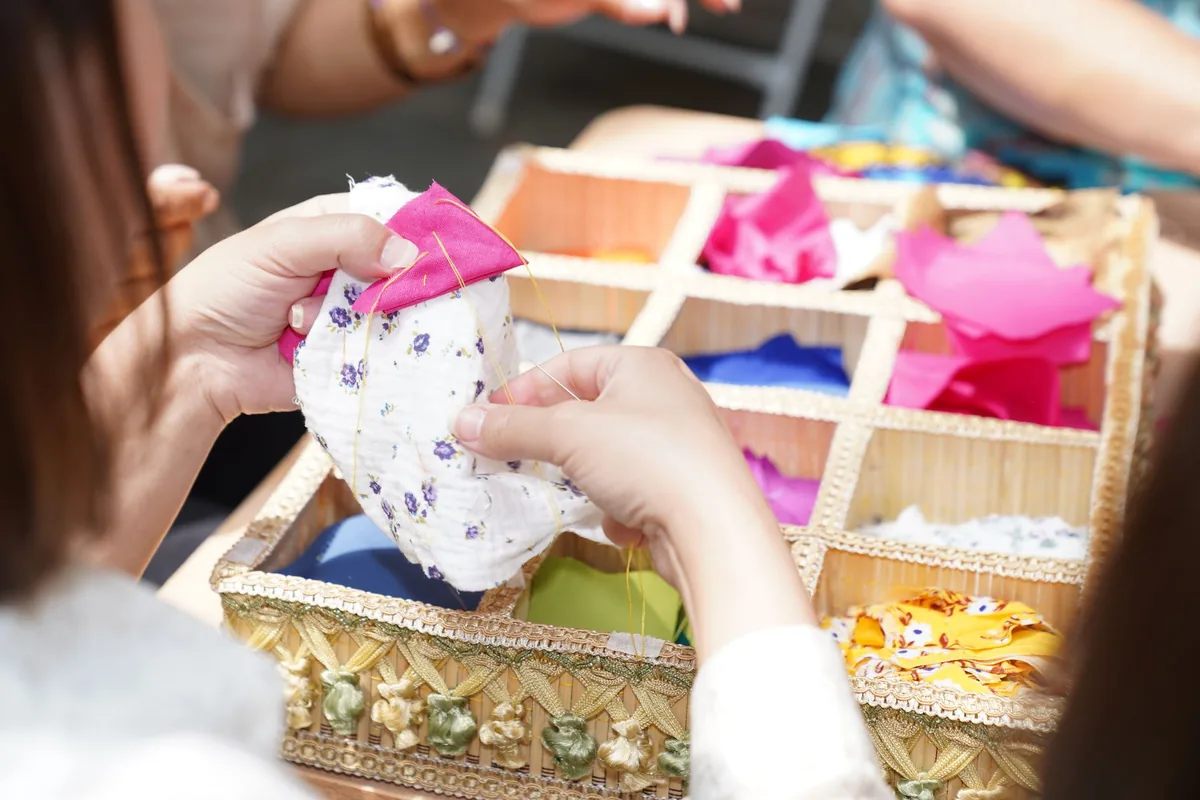 Hands sewing a piece of fabric beside a box of colourful fabric swatches