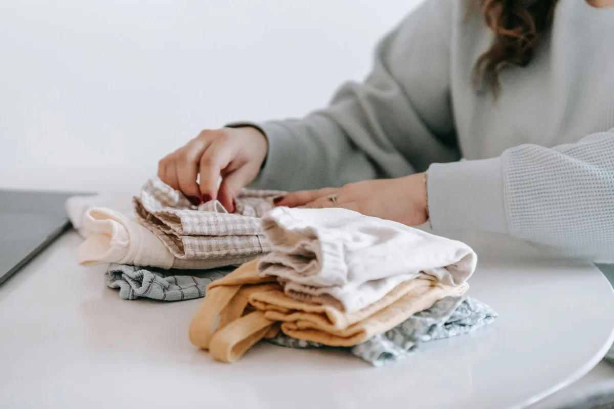 Hands folding a small stack of soft cotton clothes on a white table