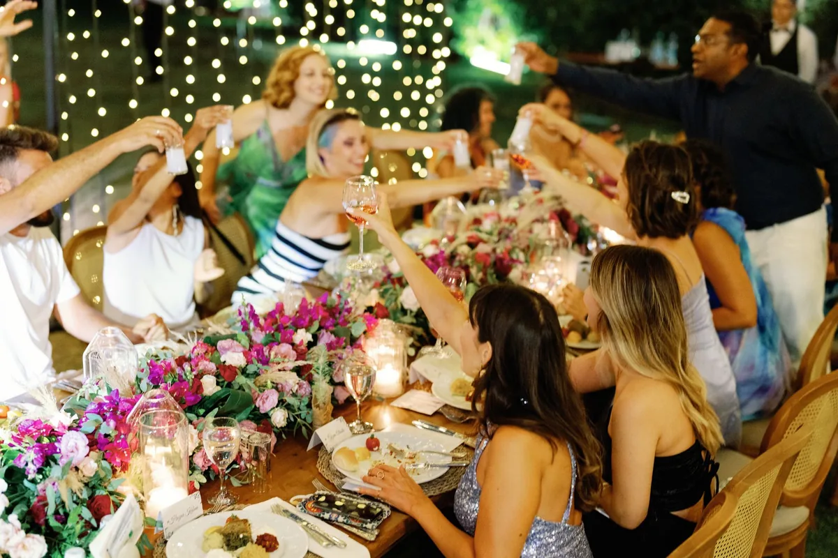 Friends raising glasses around a candlelit dinner table under string lights