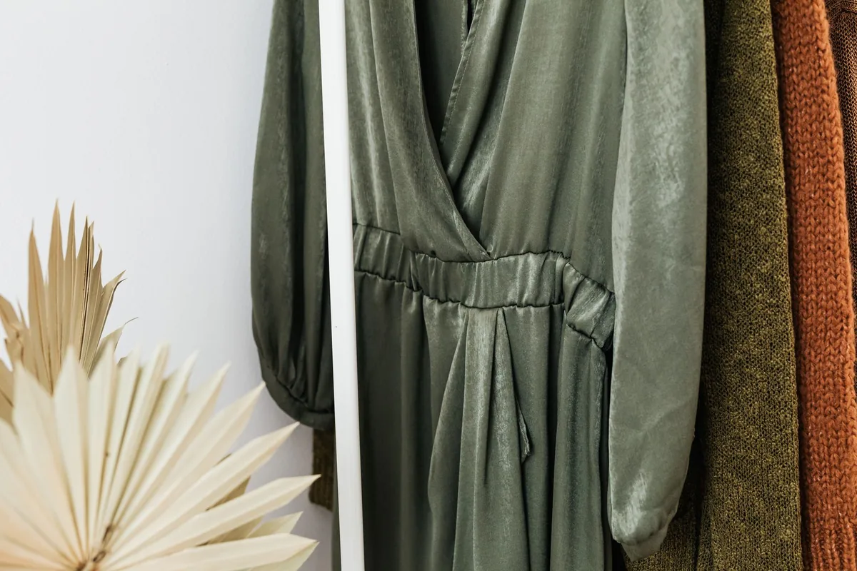 A green wrap dress hanging on a rail beside dried palm leaves