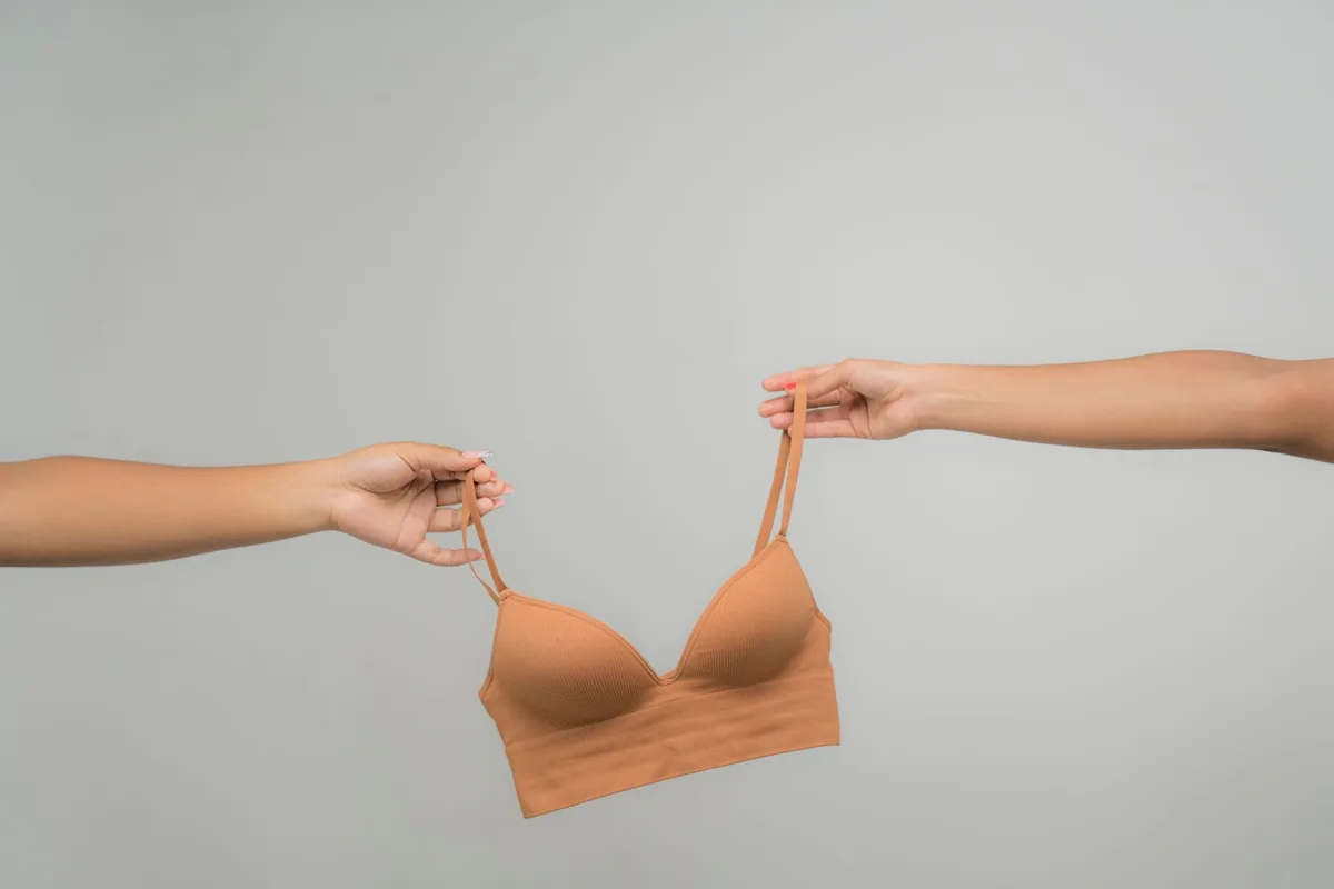 Two hands holding a nude-toned bra against a light background