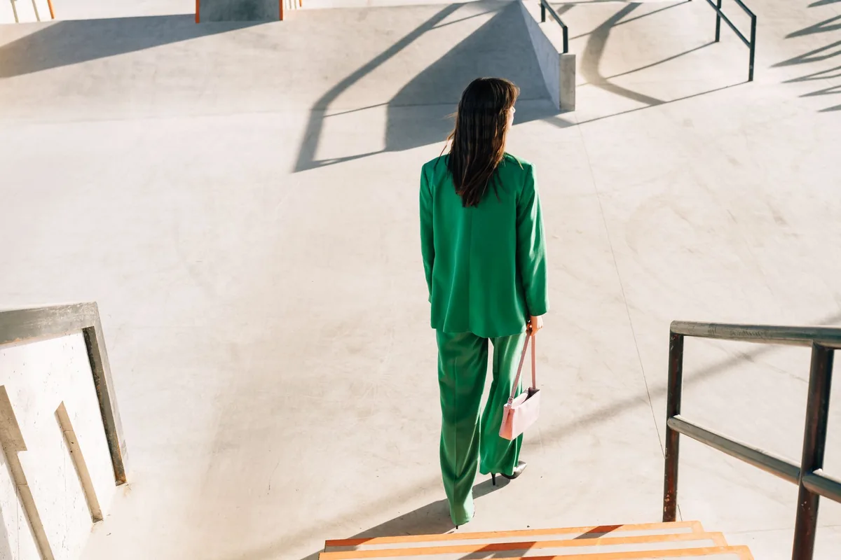 A woman in a green trouser suit climbing outdoor stairs at sunset