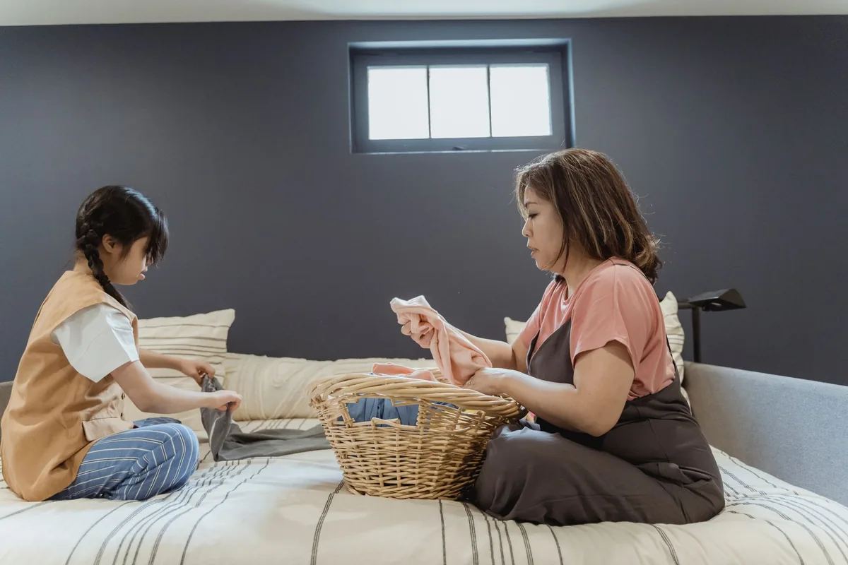 A mother and daughter folding laundry on a bed