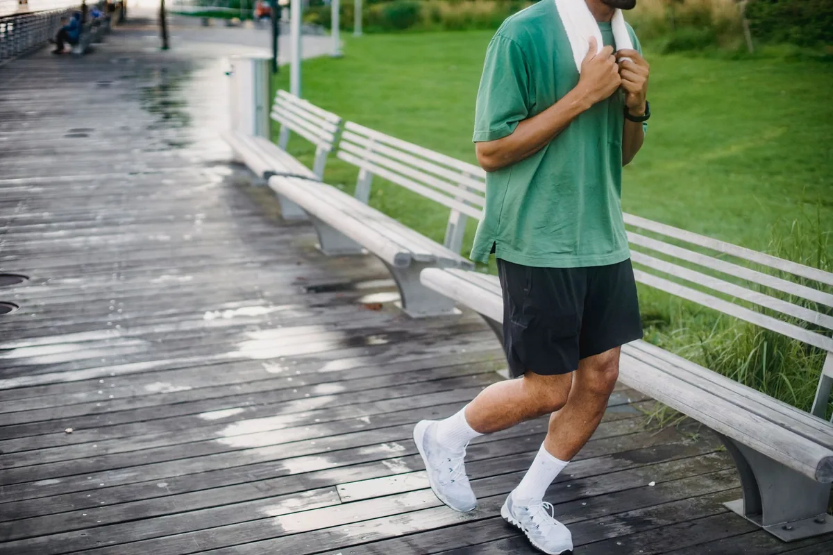 A man in a green T-shirt and dark shorts jogging past benches on a wet wooden boardwalk