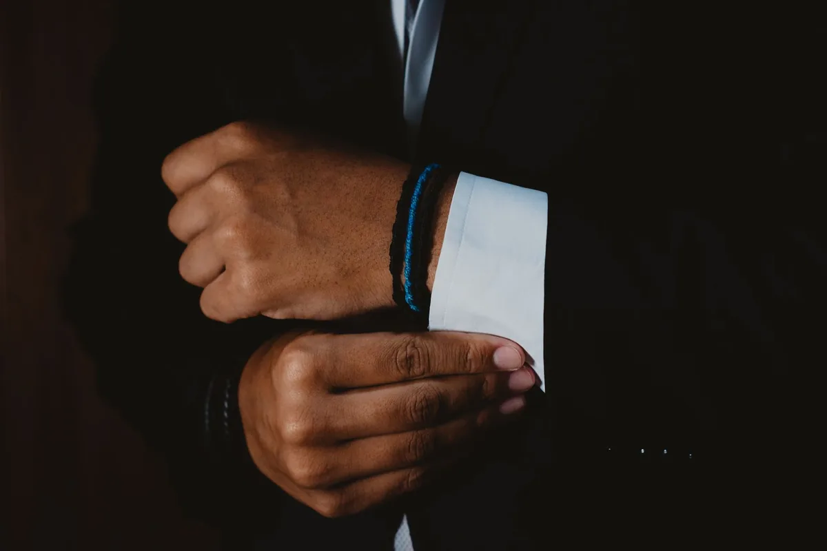 Hands fastening the white cuff of a shirt under a dark suit jacket
