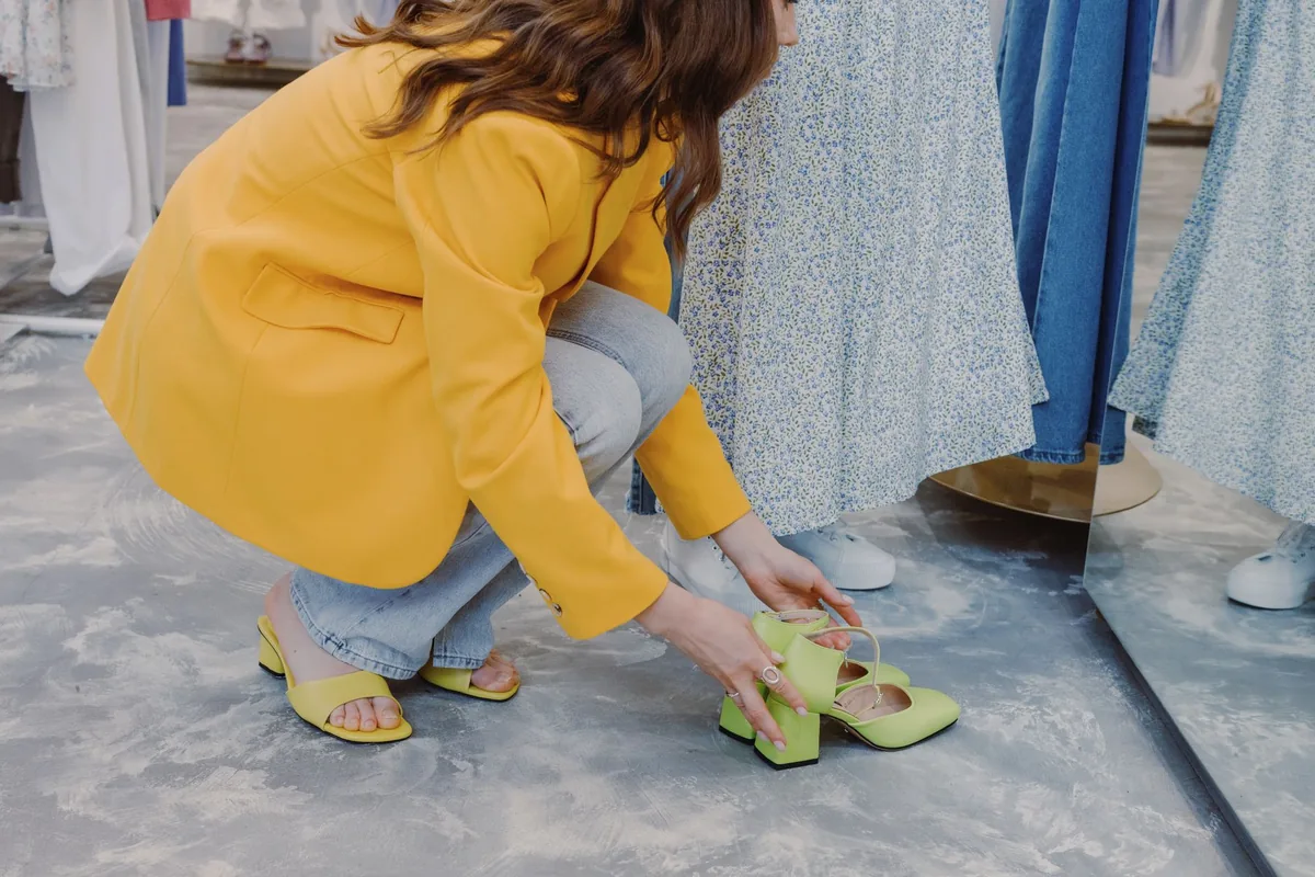 A woman crouching to try on a pair of yellow shoes in a shop
