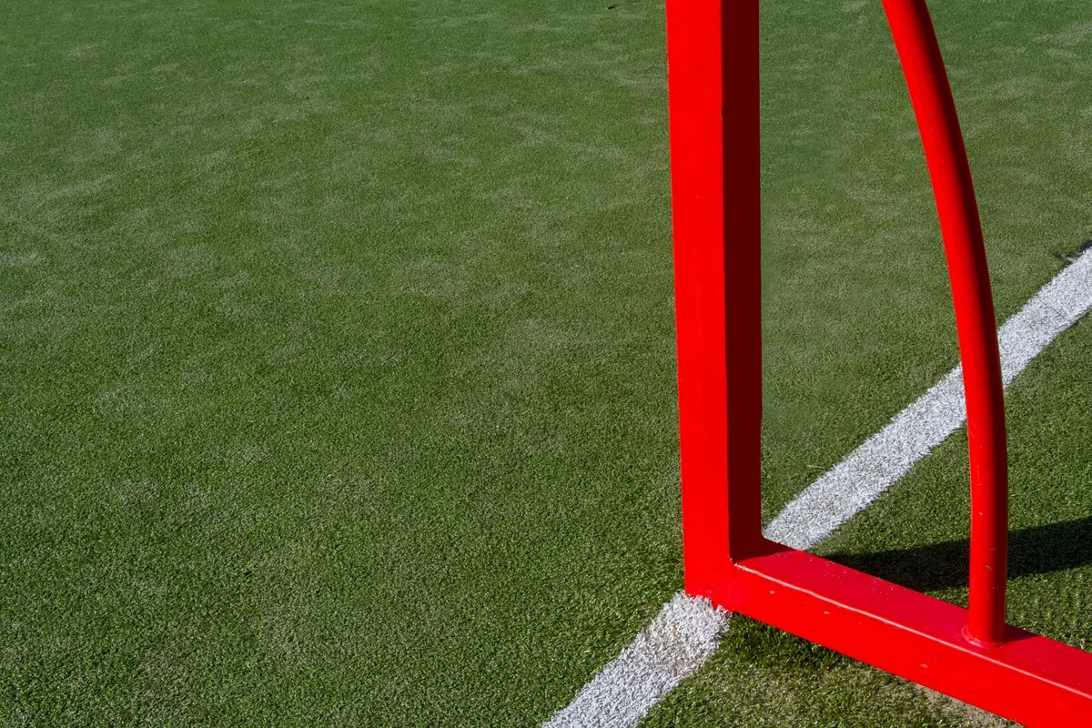 The corner of a red goal frame on a short green pitch beside a white line