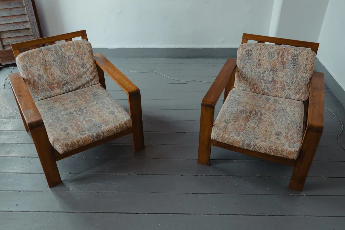 Two wooden-framed armchairs with patterned seat and back cushions on a grey painted floor