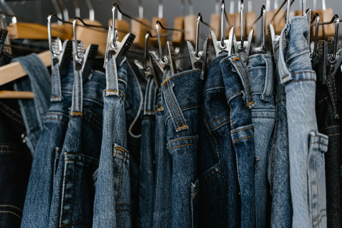 Blue jeans in several washes hanging on clip hangers on a rail