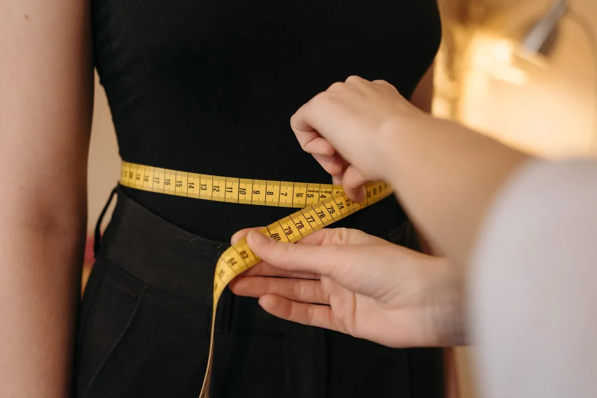 A tape measure wrapped round a woman's waist over a black top